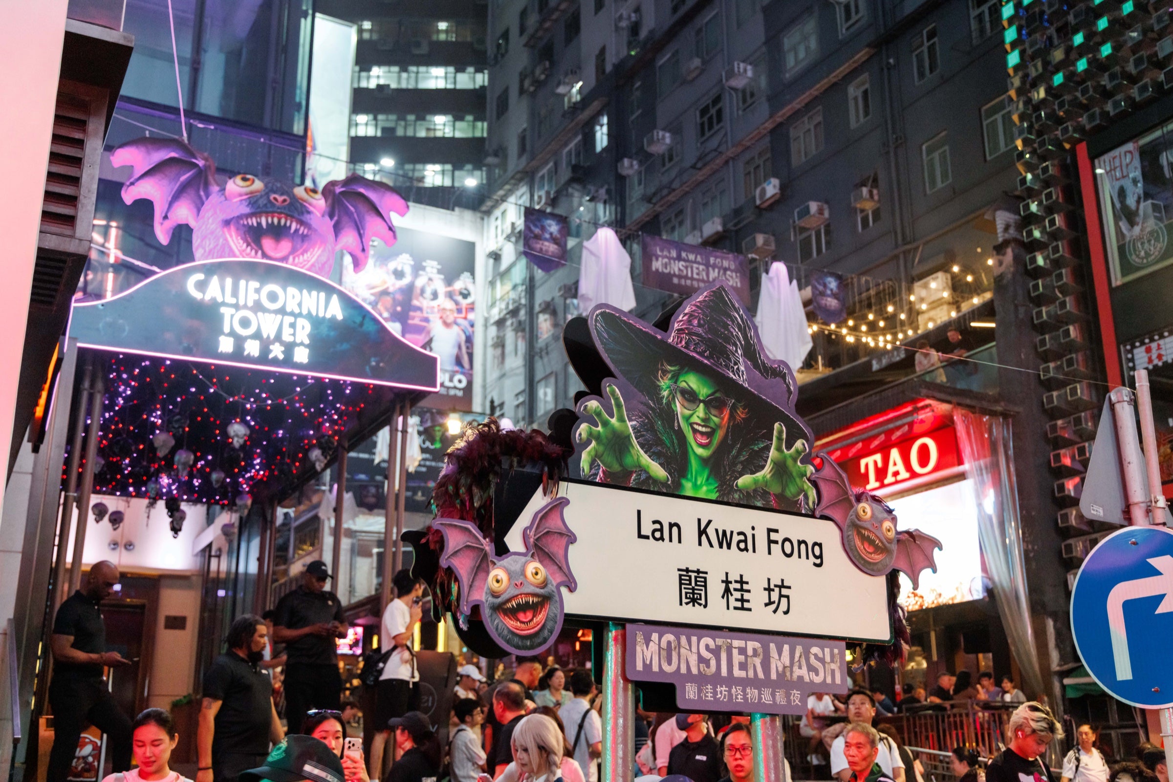 Lan Kwai Fong at night, with the California Tower sign, festive decorations, a bilingual street sign and warm street lights.